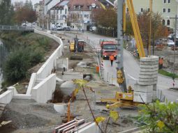 Am Floßhafen Links die Hochwasserschutzmauer mit Treppenanlage, im Baufeld Baufahrzeuge stellen die Binnenentwässerung fertig