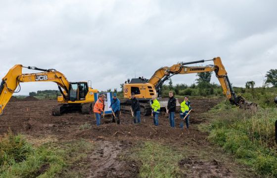 Personen mit Spaten schaufeln Erde, im Hintergrund Baumaschinen